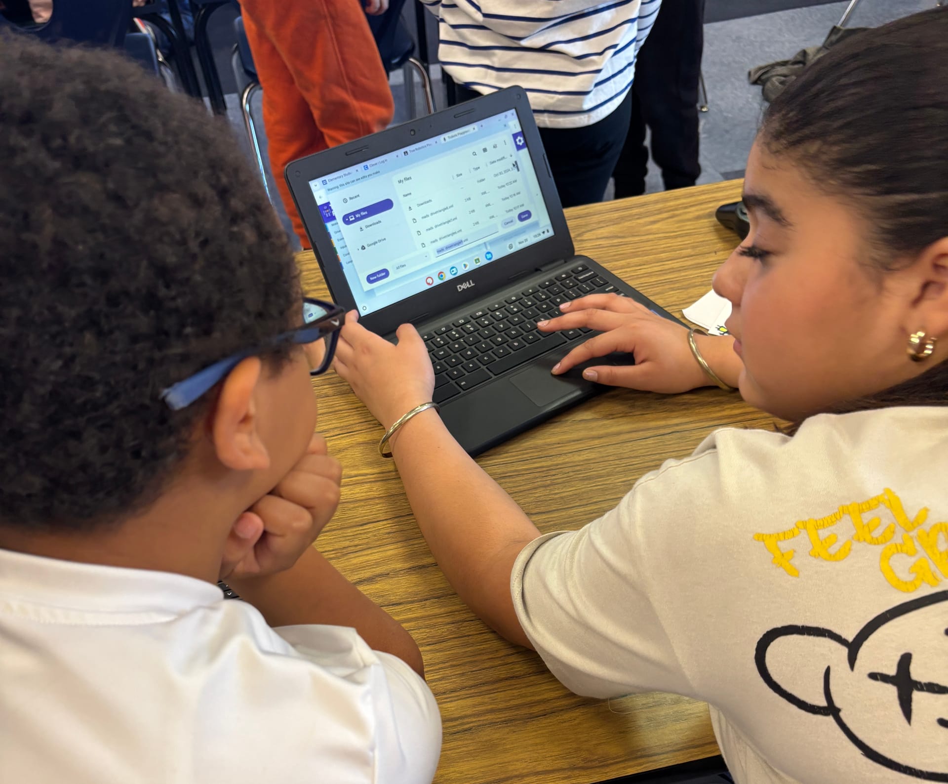 Two students lean over a Chromebook together and build a block program in True Robotics Playground