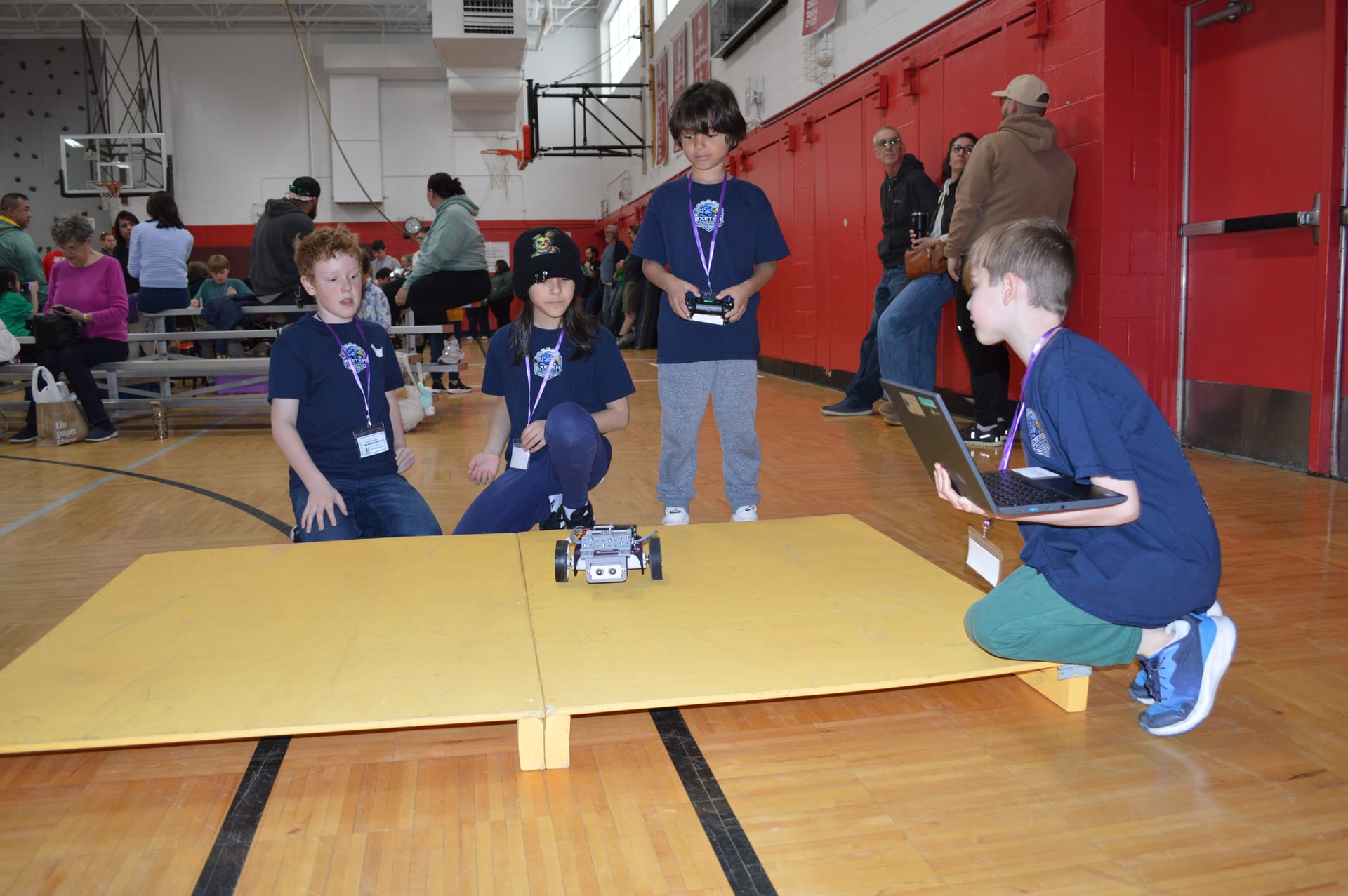 Students crouch at the edge of the yellow ramp course as their robot climbs it