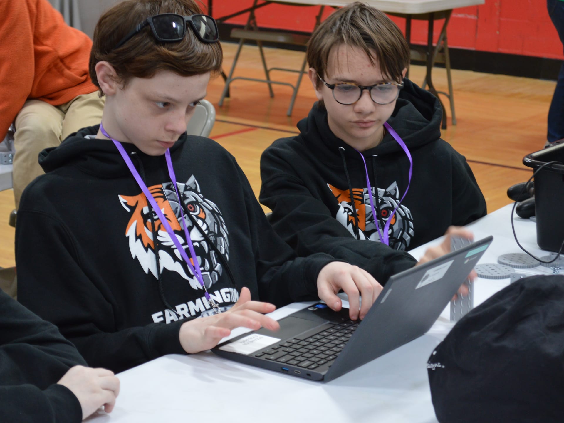 Two students in team hoodies share a laptop and write the program for their robot together