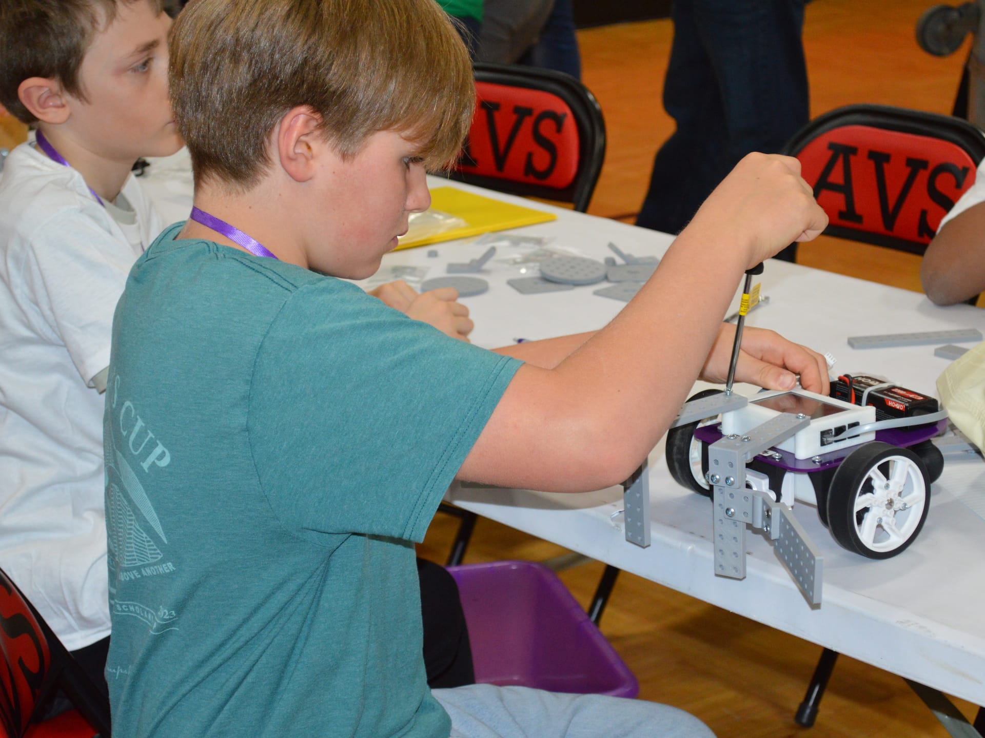 A student drives a screw into a FlexForge plow mounted on the front of a Pilot robot while a teammate works beside them