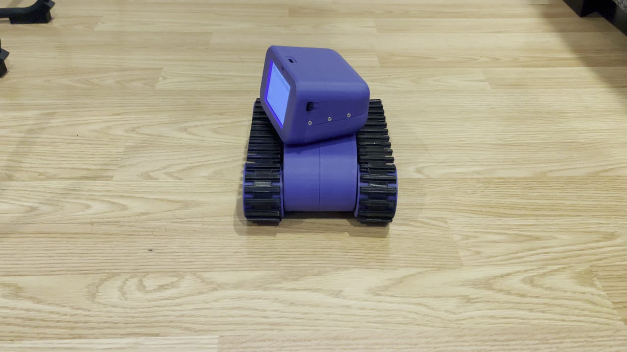 The Treads Robot turns across a wood floor while its screen shows the program it is running